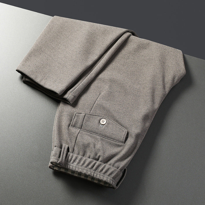 A pair of men's straight-leg casual pants in dark gray color, displayed on a model wearing white sneakers and a black top.