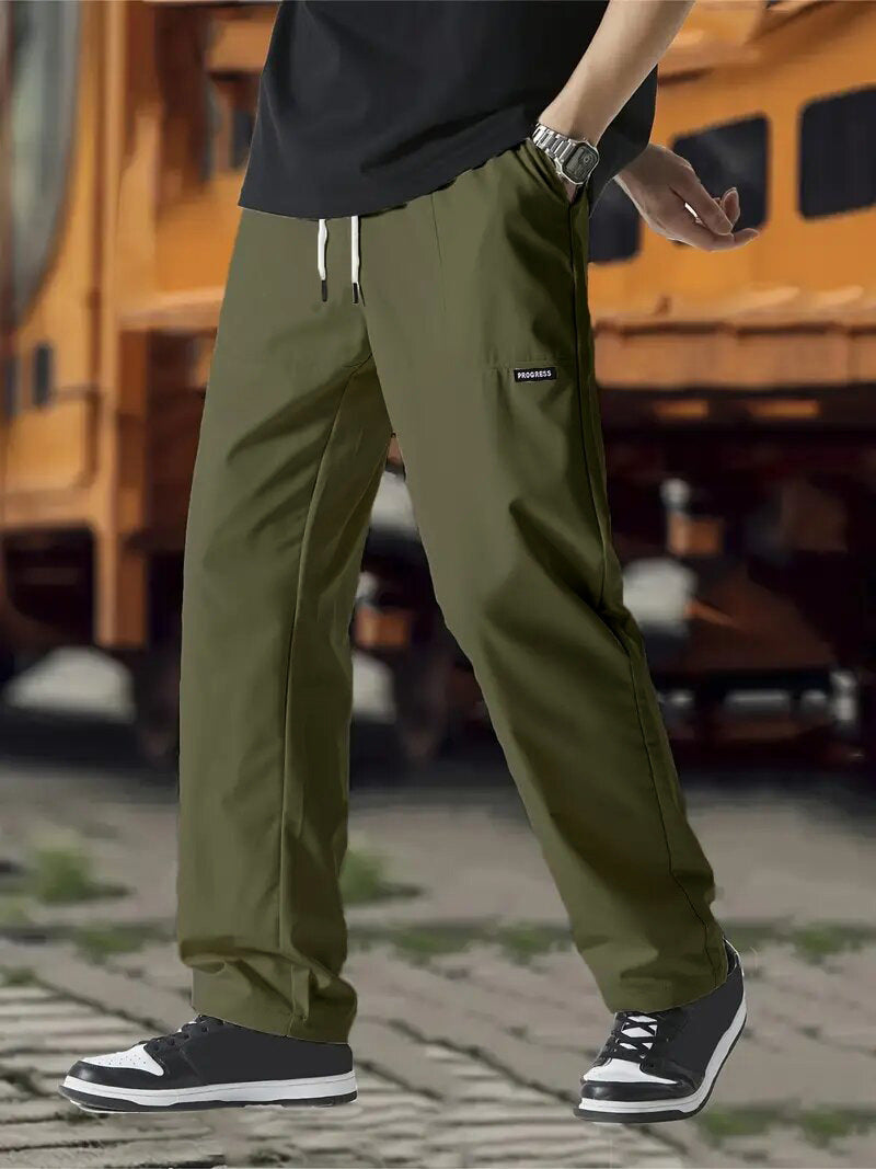 A pair of men's casual pants in green color, displayed on a model against a street backdrop.
