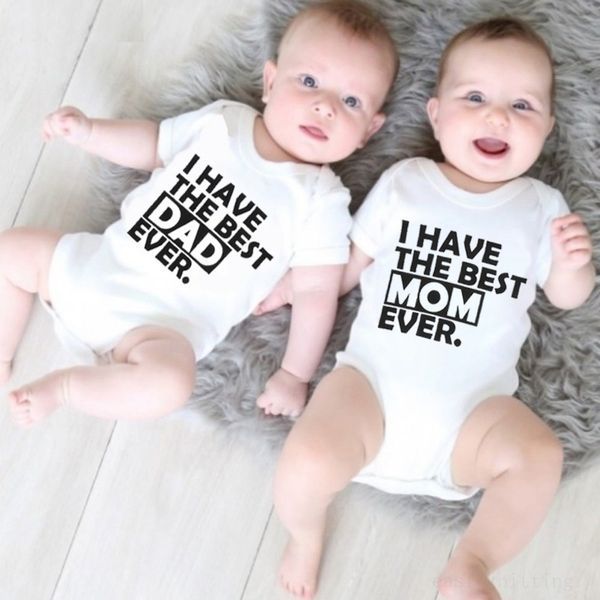 Two newborn babies lying on a furry surface, wearing white rompers with text 'I HAVE THE BEST MOM EVER' and 'I HAVE THE BEST DAD EVER' printed on them.