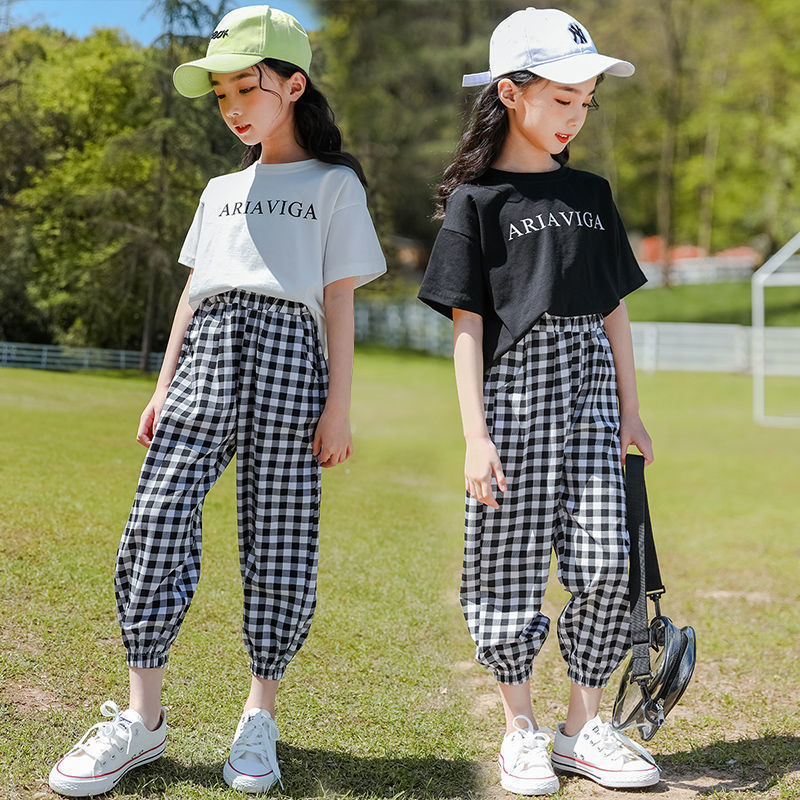Two girls wearing a summer plaid pants short sleeve suit, one with a white T-shirt and the other with a black T-shirt, both in checkered black and white pants, paired with hats and white sneakers.