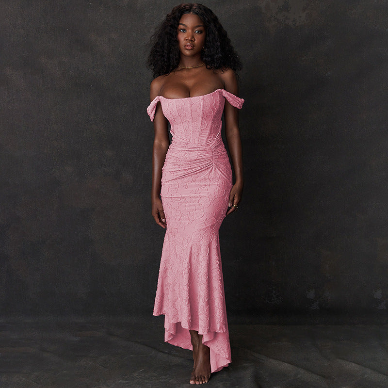 A long, sleeveless, pink evening dress with an off-shoulder neckline and a backless design, featuring a high-waist and suspender skirt.