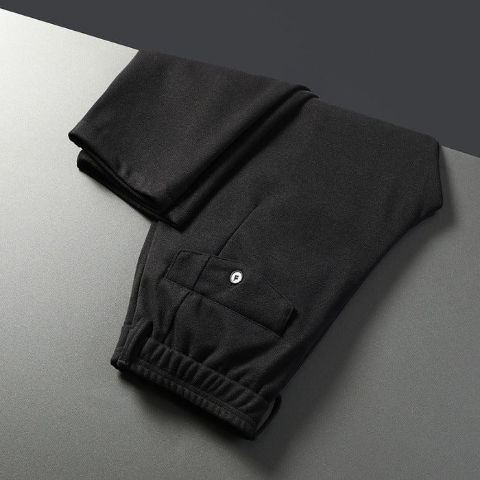 A pair of men's straight-leg casual pants in dark gray color, displayed on a model wearing white sneakers and a black top.