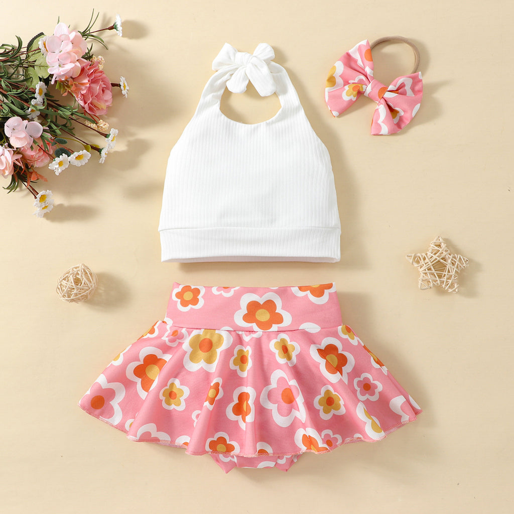 A set of children's clothing including a white sleeveless top with a bow at the neck, a pink skort with a floral pattern, and a matching hairband, displayed against a beige background with decorative elements like flowers and stars.