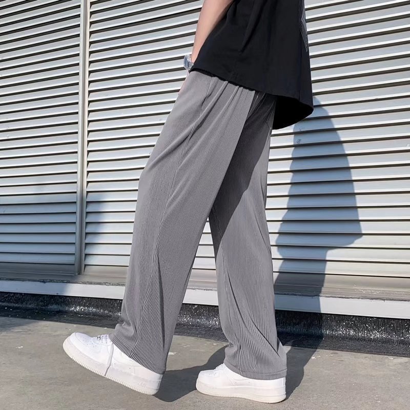 A man wearing black striped ice silk leggings and a white t-shirt, standing in front of a wall with 'FRIENDS' themed decorations.