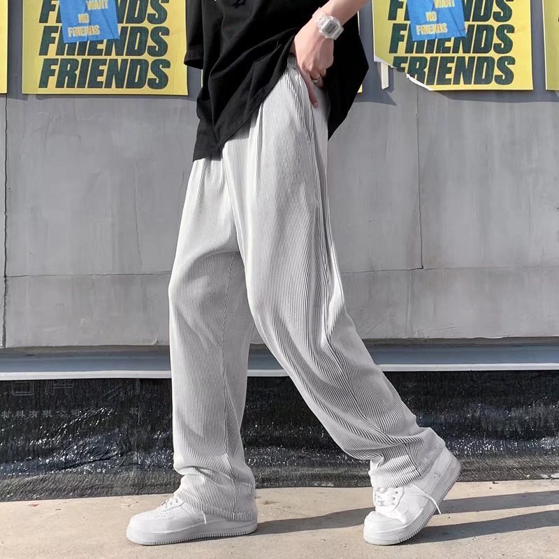 A man wearing black striped ice silk leggings and a white t-shirt, standing in front of a wall with 'FRIENDS' themed decorations.