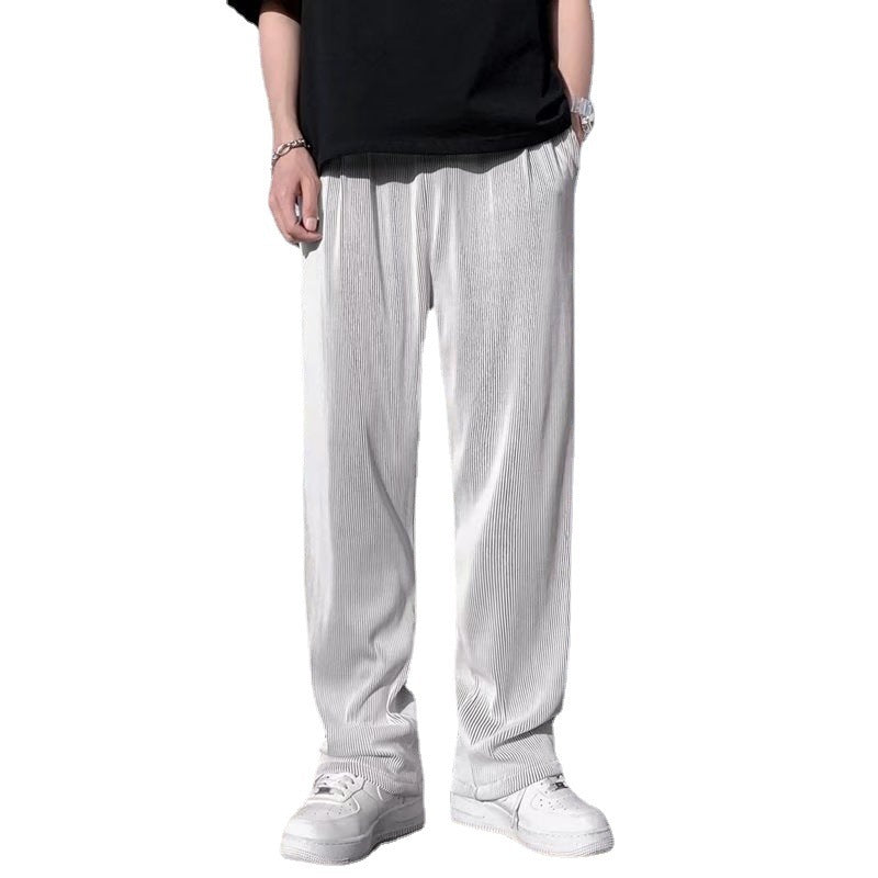 A man wearing black striped ice silk leggings and a white t-shirt, standing in front of a wall with 'FRIENDS' themed decorations.