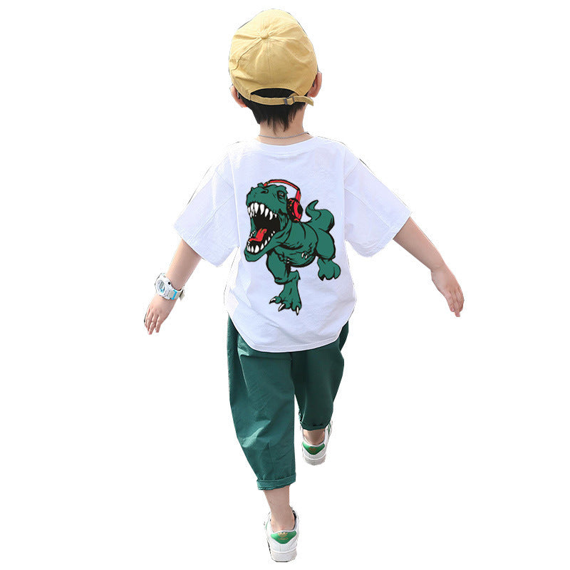 A child wearing a white short-sleeve shirt with a cartoon dinosaur print and green pants, walking away from the camera.
