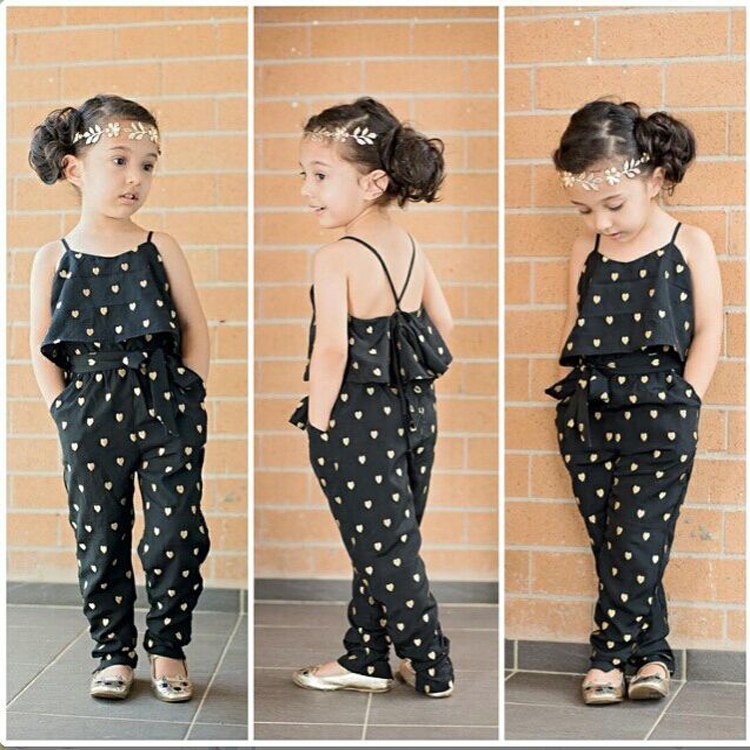 A set of three images showcasing a young girl modeling a sleeveless black jumpsuit with white polka dots. The outfits feature different views of the girl wearing a headband, standing against a brick wall background.