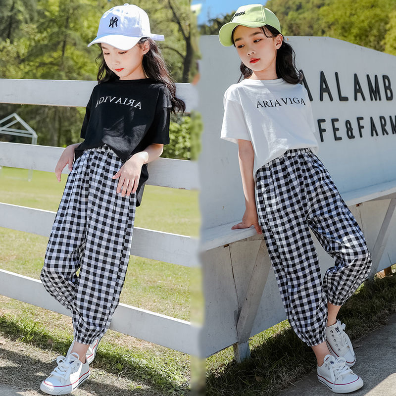 Two girls wearing a summer plaid pants short sleeve suit, one with a white T-shirt and the other with a black T-shirt, both in checkered black and white pants, paired with hats and white sneakers.