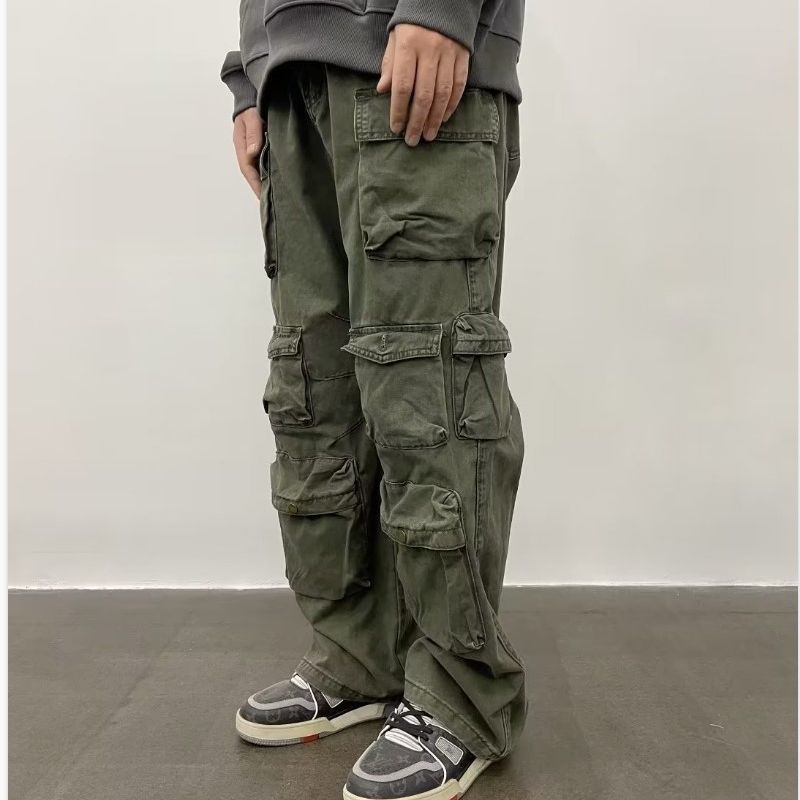 A person standing against a white background, wearing army green straight-leg casual pants with multiple pockets and a pair of sneakers.