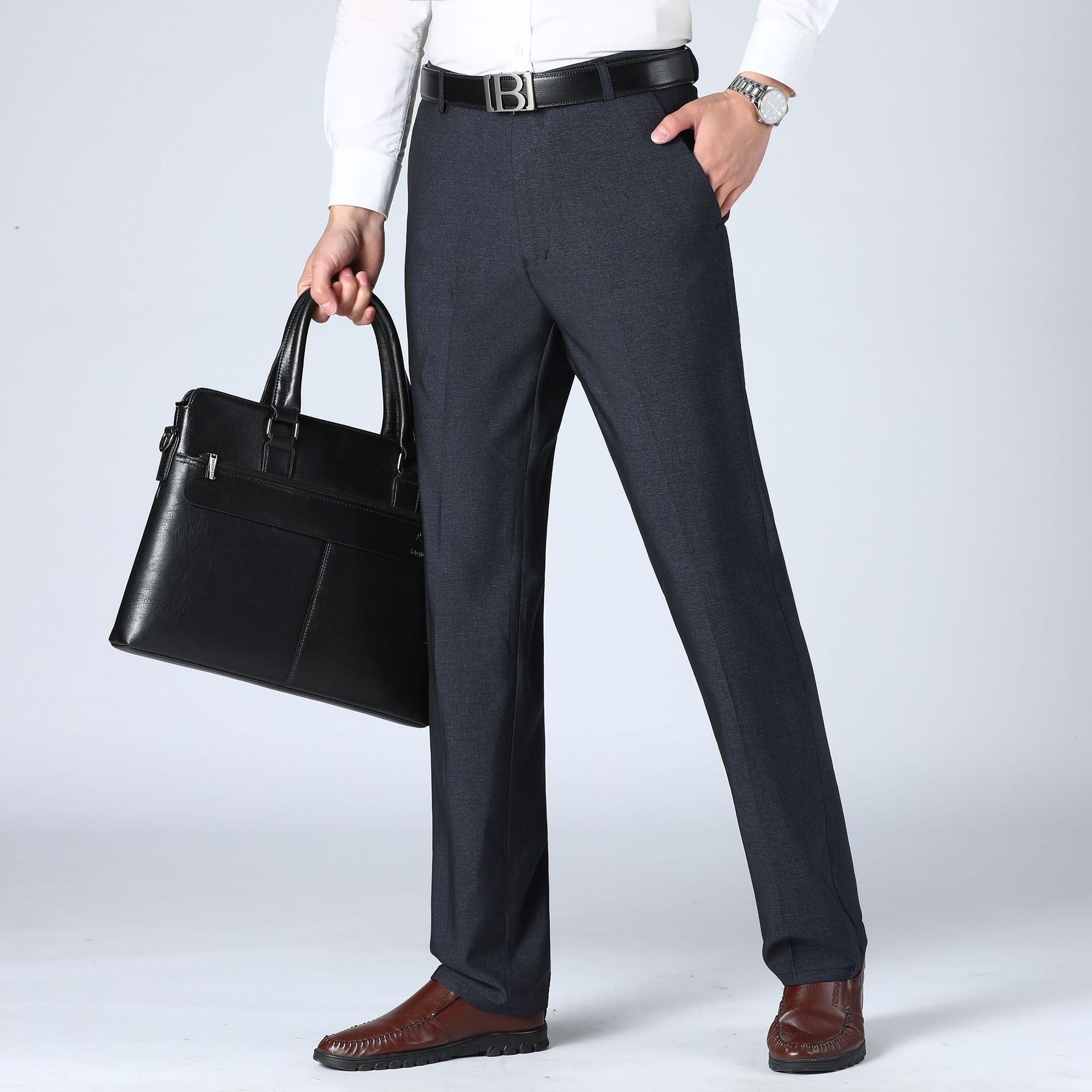 A pair of men's straight-leg suit pants in a light gray color, displayed in a full-length image with a person standing with one hand in a pocket.