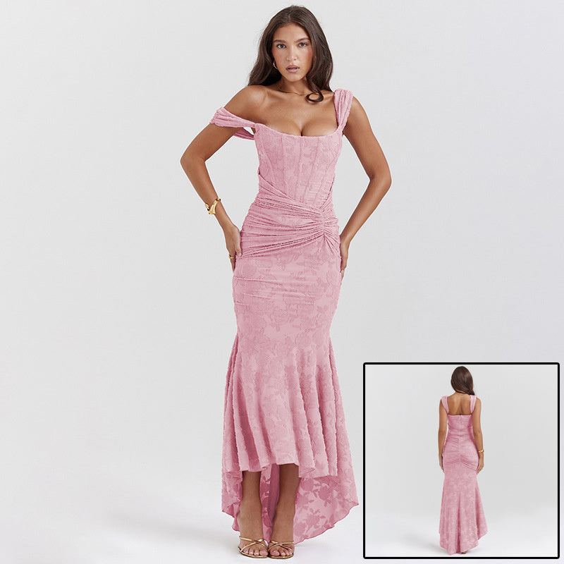 A long, sleeveless, pink evening dress with an off-shoulder neckline and a backless design, featuring a high-waist and suspender skirt.
