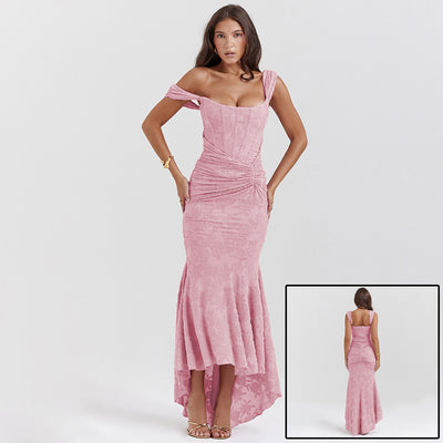 A long, sleeveless, pink evening dress with an off-shoulder neckline and a backless design, featuring a high-waist and suspender skirt.