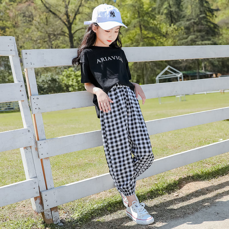 Two girls wearing a summer plaid pants short sleeve suit, one with a white T-shirt and the other with a black T-shirt, both in checkered black and white pants, paired with hats and white sneakers.