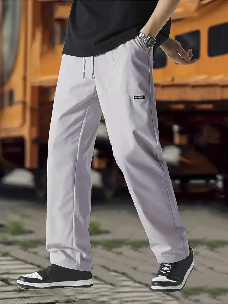 A pair of men's casual pants in green color, displayed on a model against a street backdrop.