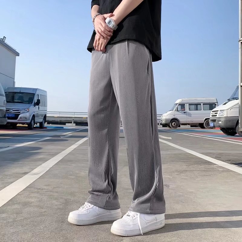A man wearing black striped ice silk leggings and a white t-shirt, standing in front of a wall with 'FRIENDS' themed decorations.
