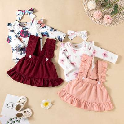 Three-piece baby girl outfit set featuring floral long-sleeved top, solid color wine red and pink ruffled dresses, and matching headdress. 