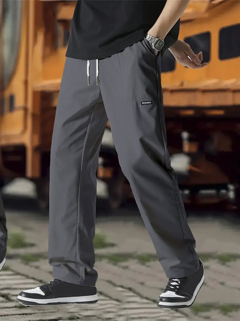 A pair of men's casual pants in green color, displayed on a model against a street backdrop.
