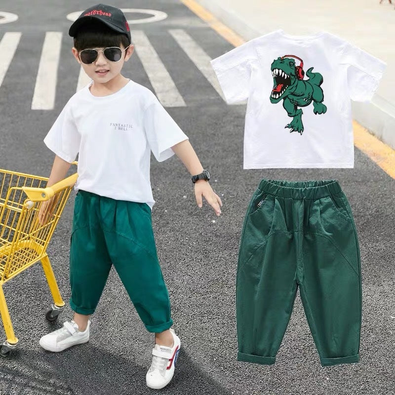 A child wearing a white short-sleeve shirt with a cartoon dinosaur print and green pants, walking away from the camera.