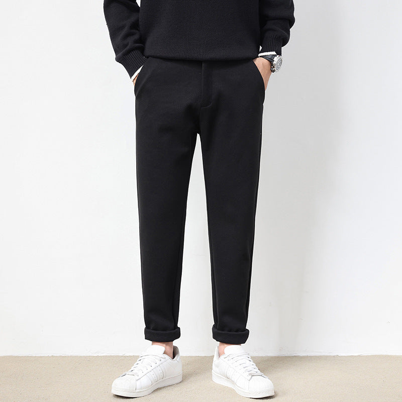 A pair of men's straight-leg casual pants in dark gray color, displayed on a model wearing white sneakers and a black top.