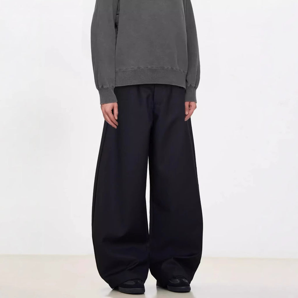 A person standing against a white background, wearing black wide-leg suit pants and a gray sweatshirt.