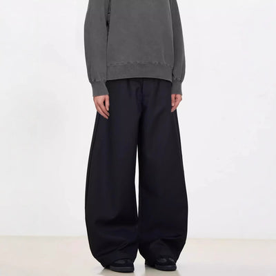 A person standing against a white background, wearing black wide-leg suit pants and a gray sweatshirt.