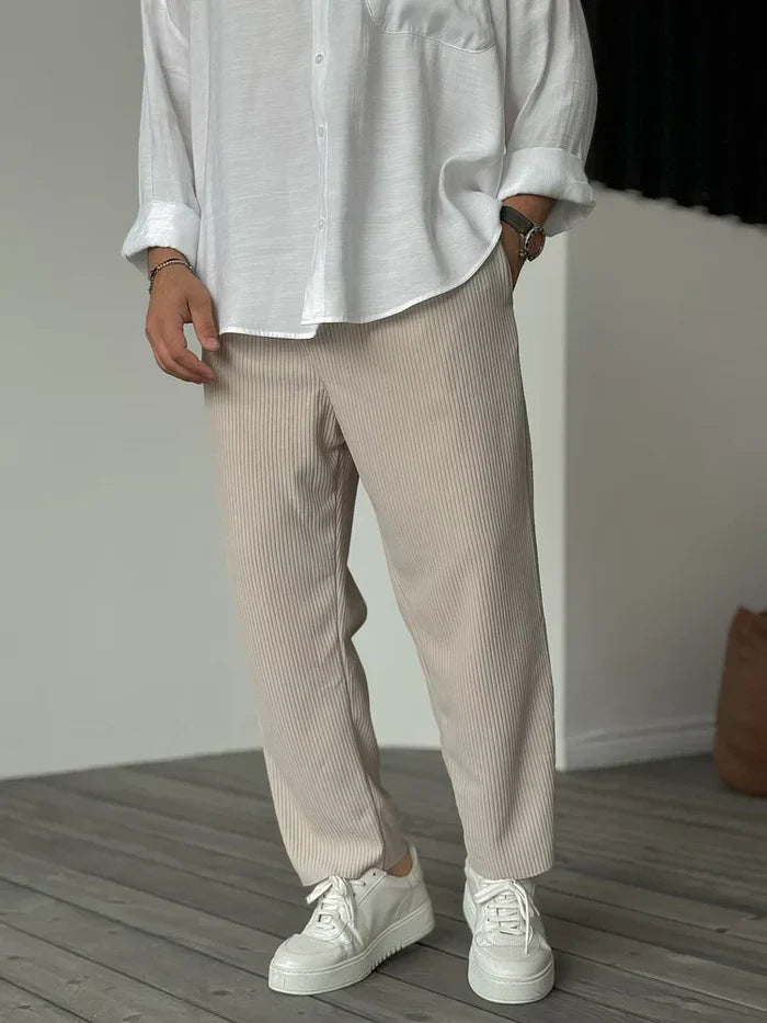 A person wearing loose straight sports casual pants with a striped pattern, in colors white, gray, and black, paired with a white shirt and white sneakers.