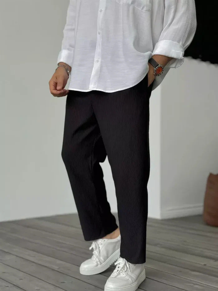 A person wearing loose straight sports casual pants with a striped pattern, in colors white, gray, and black, paired with a white shirt and white sneakers.