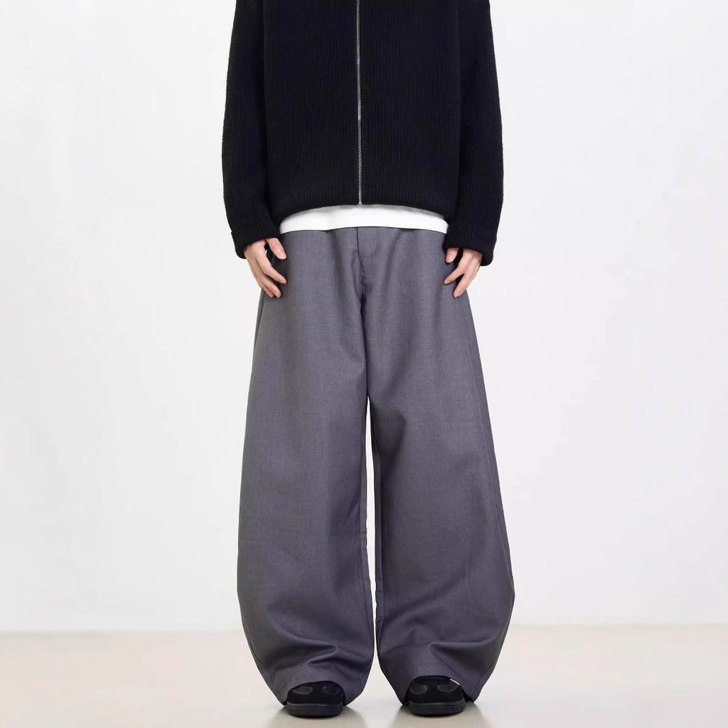 A person standing against a white background, wearing black wide-leg suit pants and a gray sweatshirt.