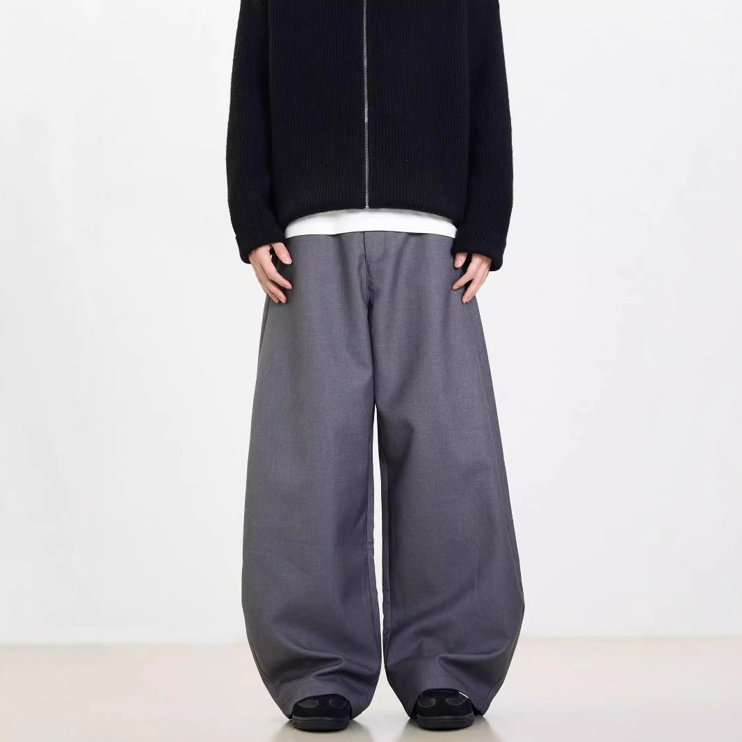 A person standing against a white background, wearing black wide-leg suit pants and a gray sweatshirt.