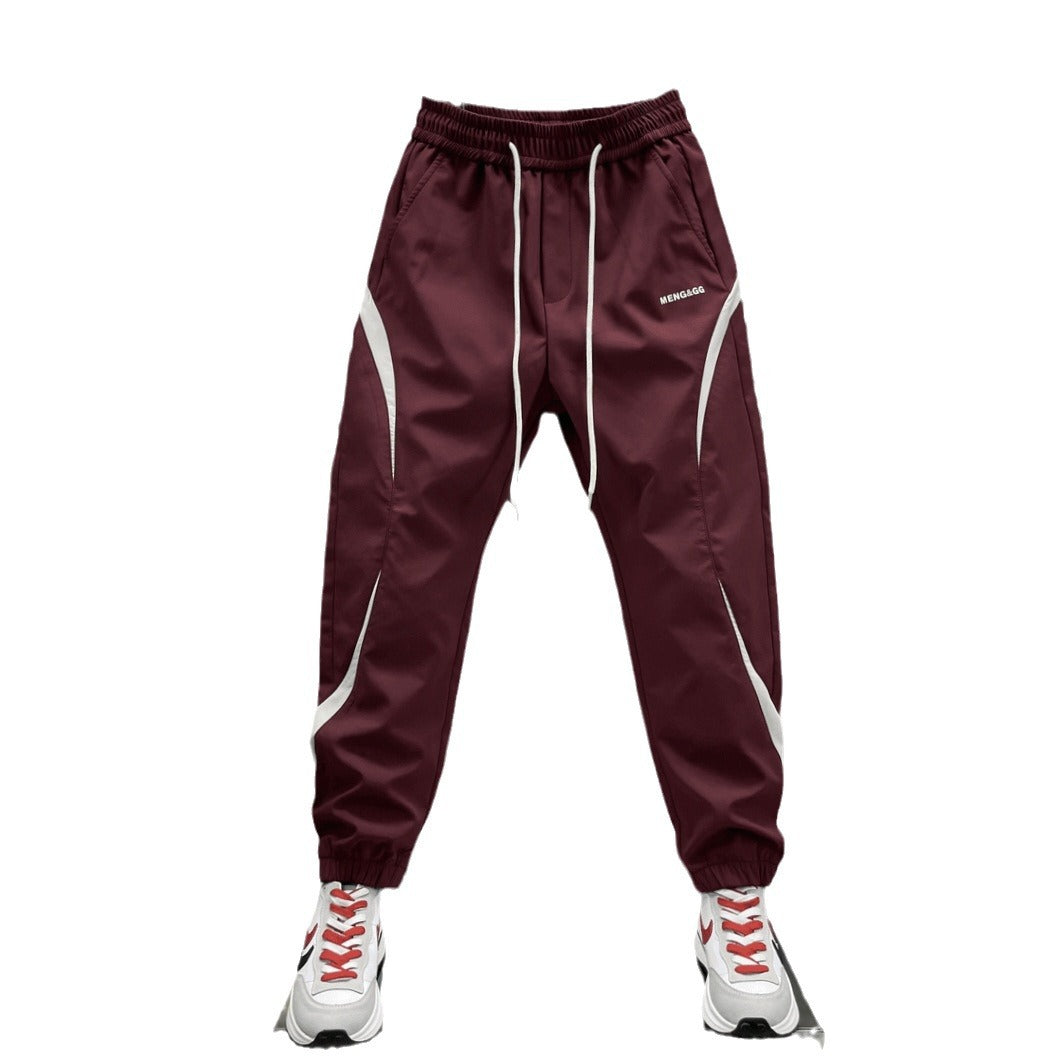 Two pairs of ankle banded pants displayed, one in white and one in wine red, both with drawstrings and side stripes, suitable for youth sizes.