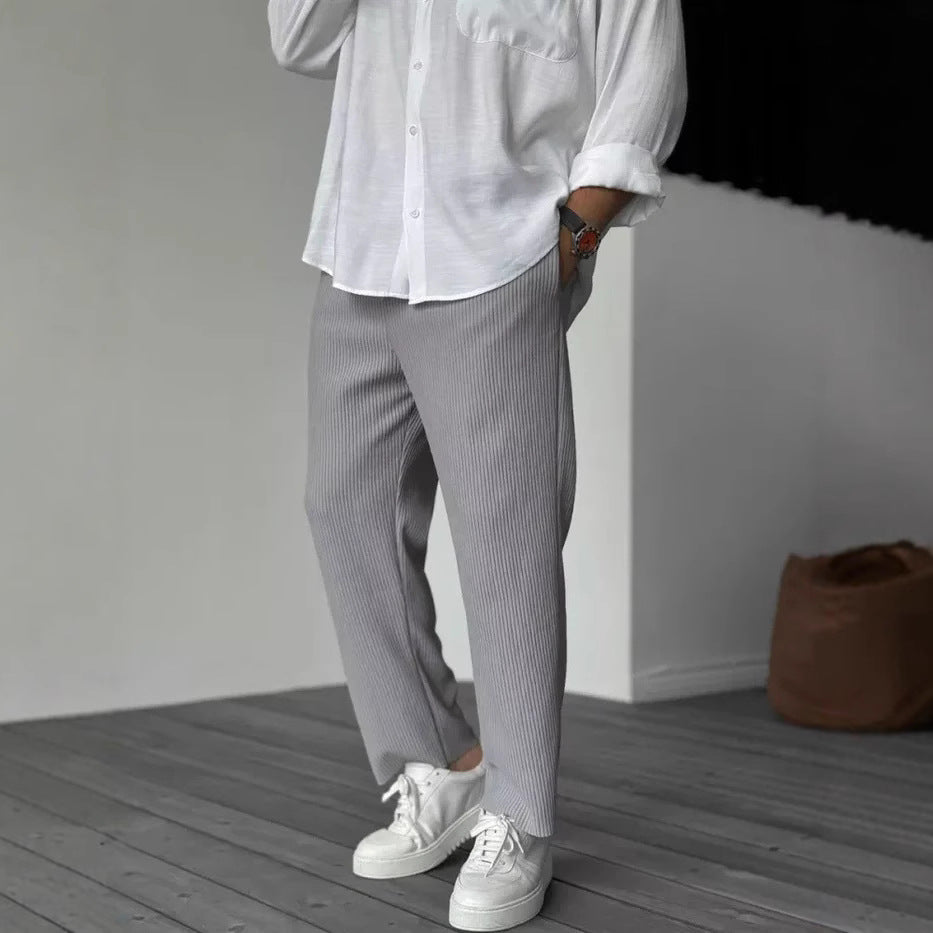 A person wearing loose straight sports casual pants with a striped pattern, in colors white, gray, and black, paired with a white shirt and white sneakers.