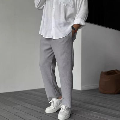A person wearing loose straight sports casual pants with a striped pattern, in colors white, gray, and black, paired with a white shirt and white sneakers.