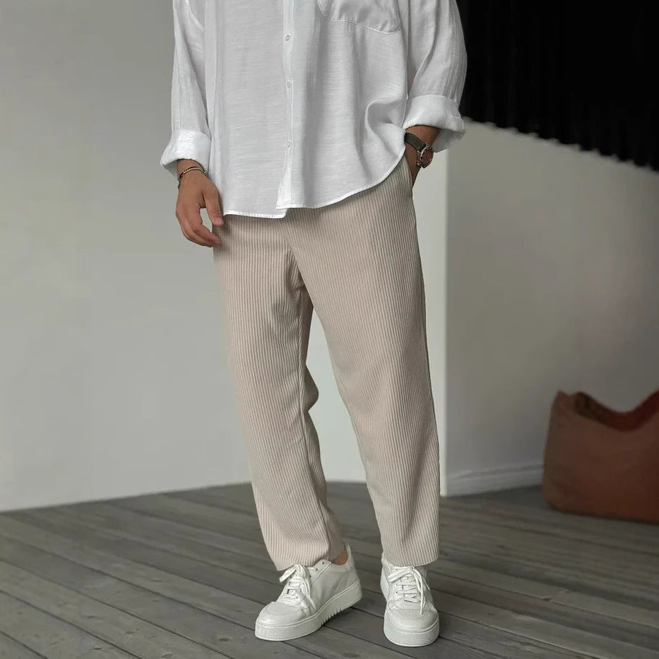 A person wearing loose straight sports casual pants with a striped pattern, in colors white, gray, and black, paired with a white shirt and white sneakers.