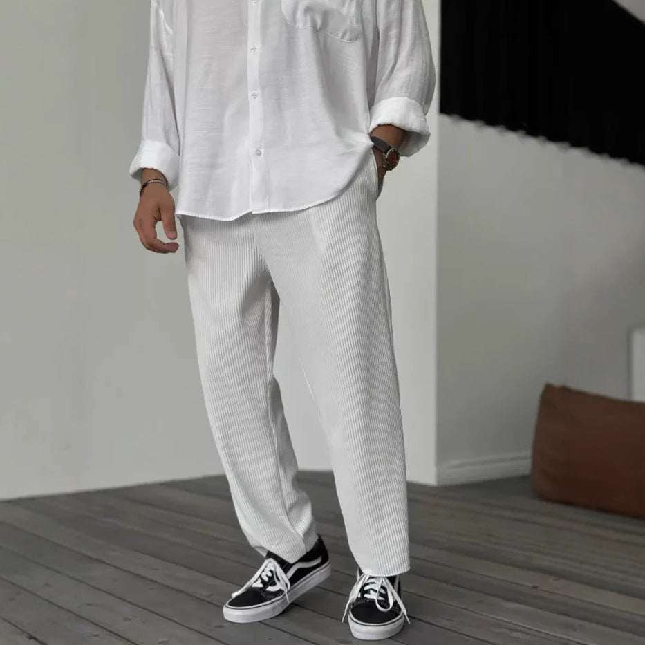 A person wearing loose straight sports casual pants with a striped pattern, in colors white, gray, and black, paired with a white shirt and white sneakers.