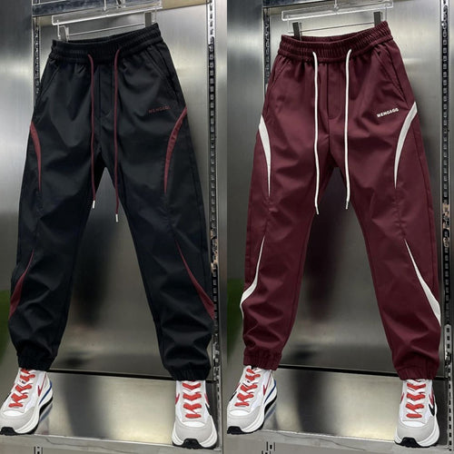 Two pairs of ankle banded pants displayed, one in white and one in wine red, both with drawstrings and side stripes, suitable for youth sizes.