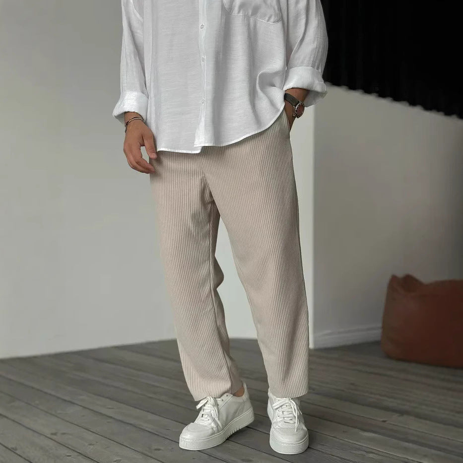 A person wearing loose straight sports casual pants with a striped pattern, in colors white, gray, and black, paired with a white shirt and white sneakers.