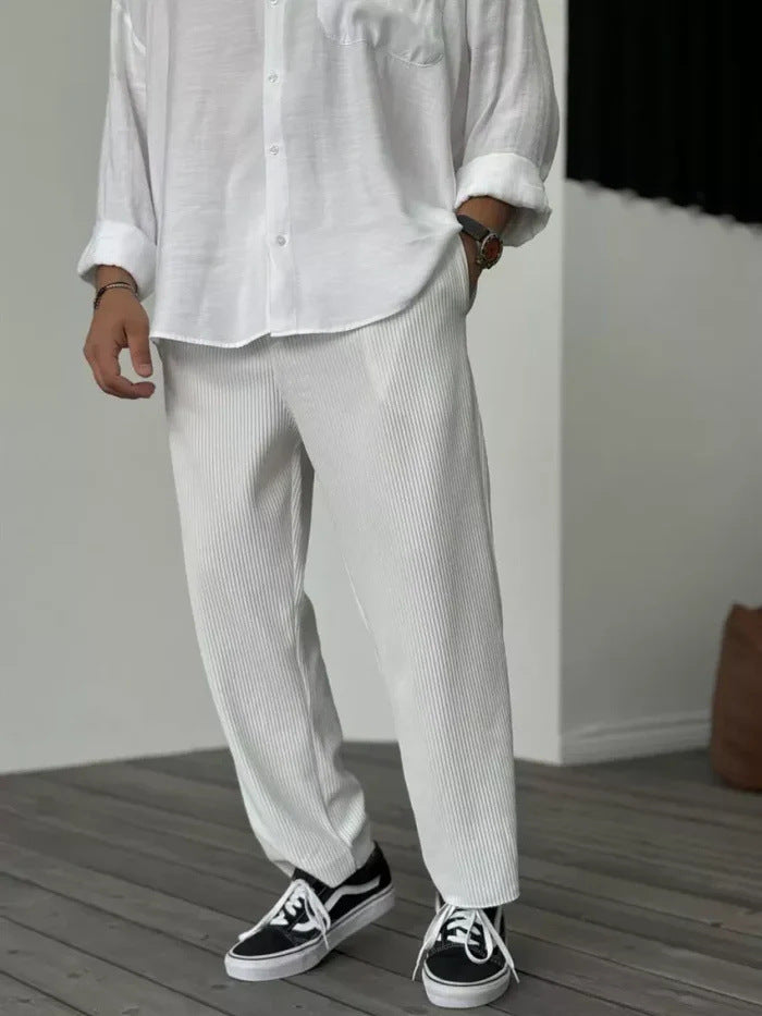 A person wearing loose straight sports casual pants with a striped pattern, in colors white, gray, and black, paired with a white shirt and white sneakers.