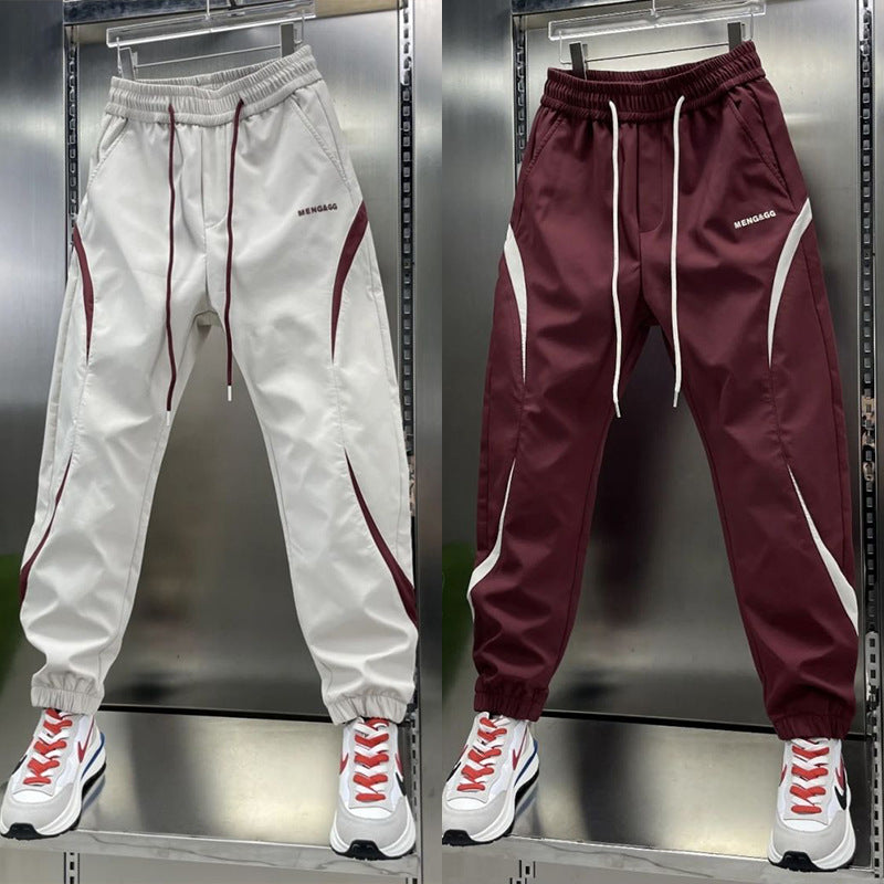 Two pairs of ankle banded pants displayed, one in white and one in wine red, both with drawstrings and side stripes, suitable for youth sizes.