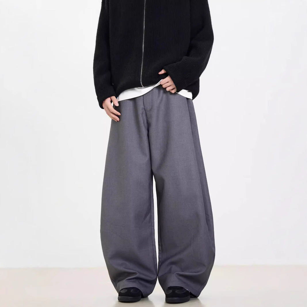 A person standing against a white background, wearing black wide-leg suit pants and a gray sweatshirt.