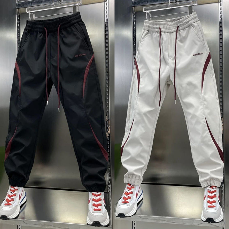 Two pairs of ankle banded pants displayed, one in white and one in wine red, both with drawstrings and side stripes, suitable for youth sizes.