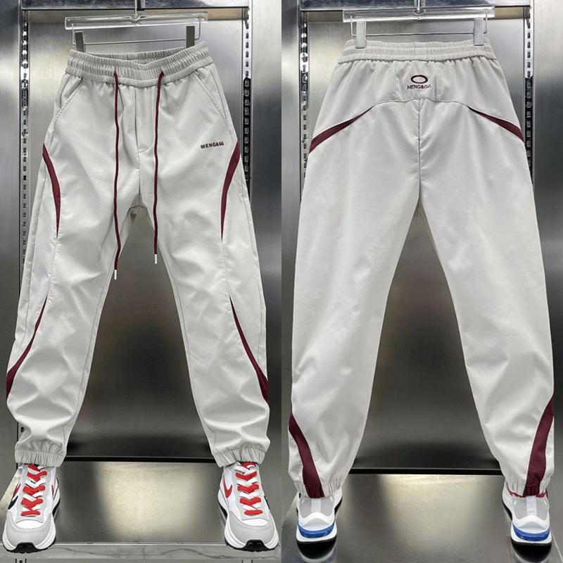 Two pairs of ankle banded pants displayed, one in white and one in wine red, both with drawstrings and side stripes, suitable for youth sizes.