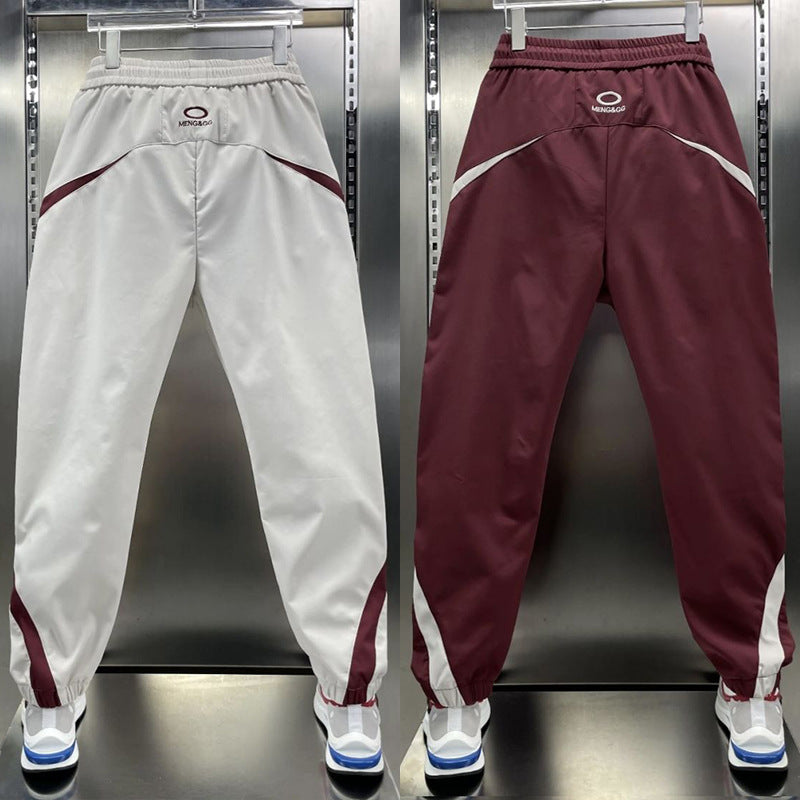 Two pairs of ankle banded pants displayed, one in white and one in wine red, both with drawstrings and side stripes, suitable for youth sizes.