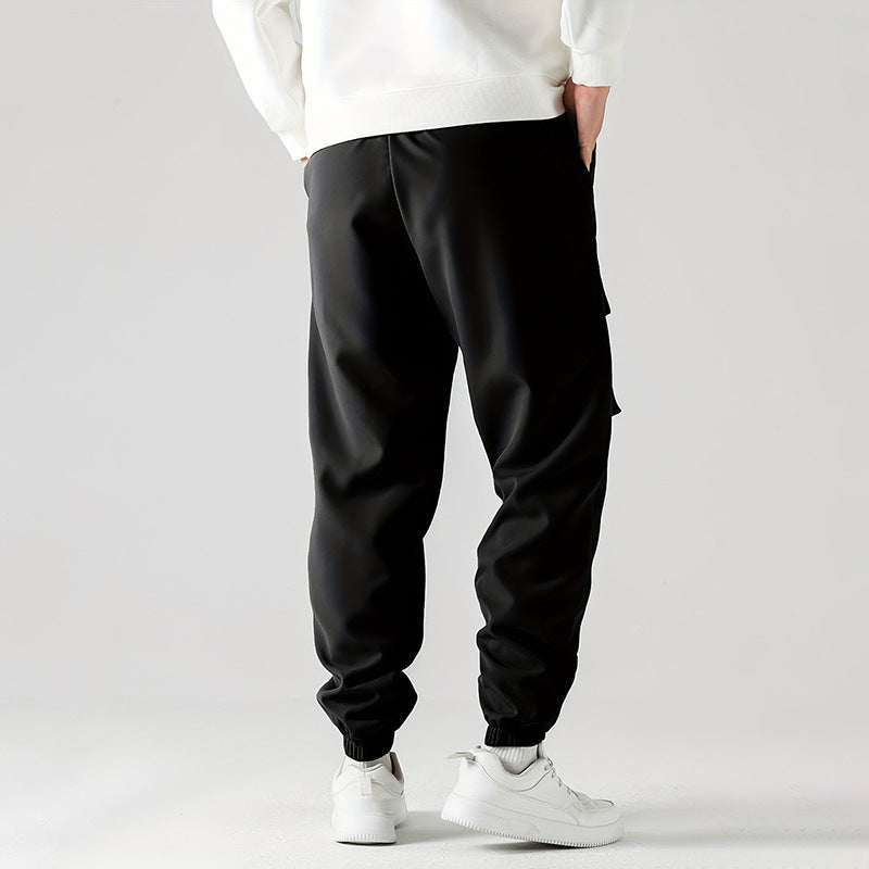 A person wearing black straight-leg ankle-tied overalls casual pants with a mid-waist waist and white sneakers.