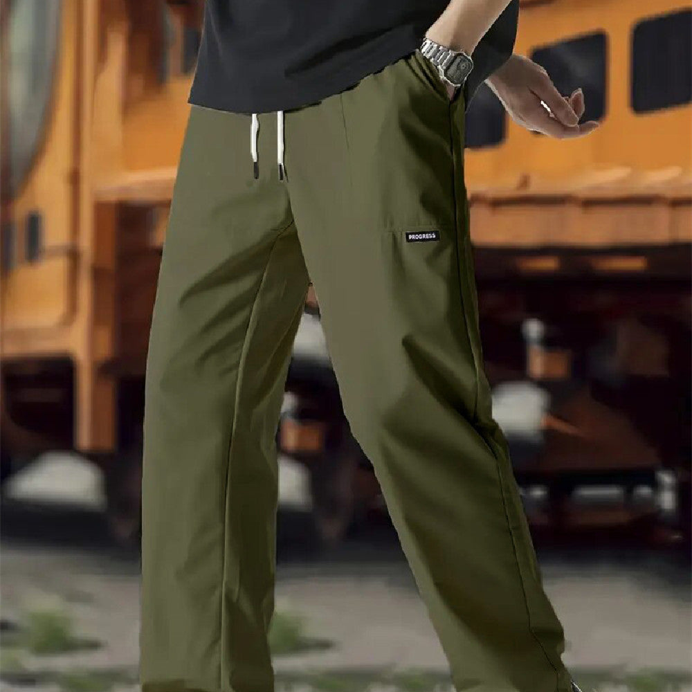 A pair of men's casual pants in green color, displayed on a model against a street backdrop.