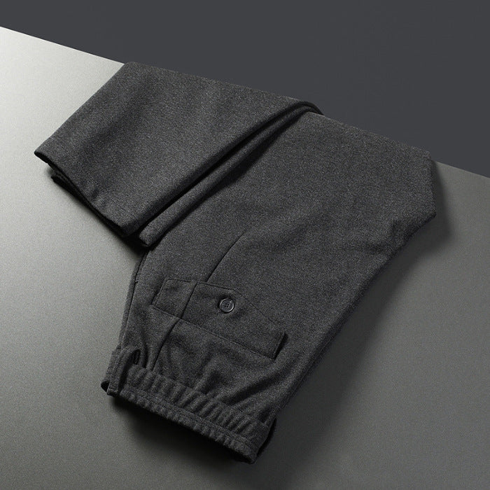 A pair of men's straight-leg casual pants in dark gray color, displayed on a model wearing white sneakers and a black top.