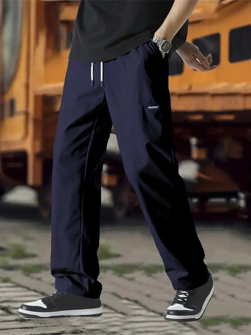 A pair of men's casual pants in green color, displayed on a model against a street backdrop.