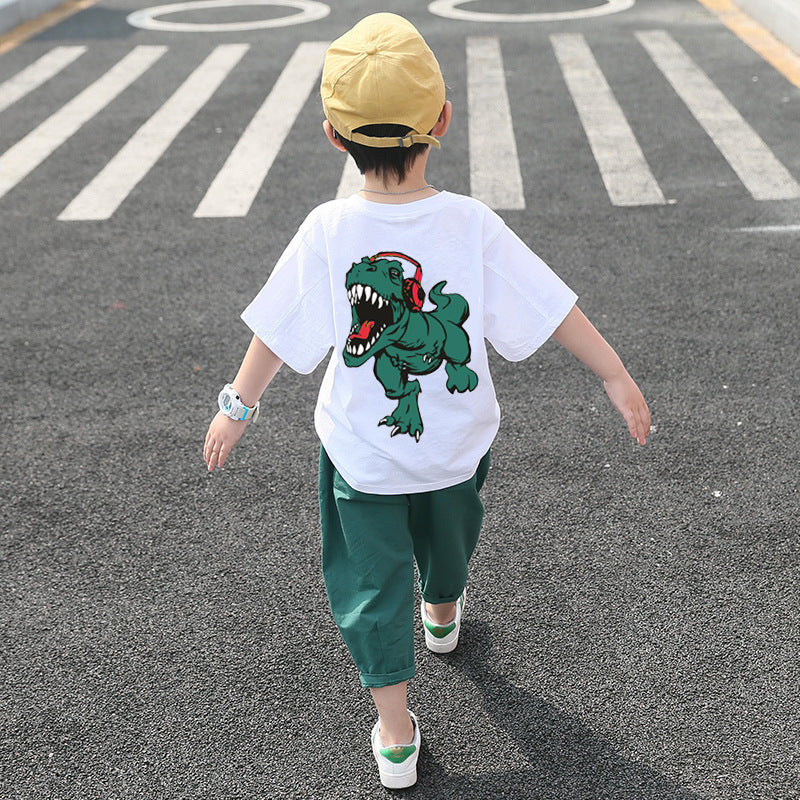 A child wearing a white short-sleeve shirt with a cartoon dinosaur print and green pants, walking away from the camera.