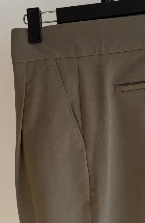 A person standing in an indoor setting wearing high waist slim fit business casual trousers in a green color.