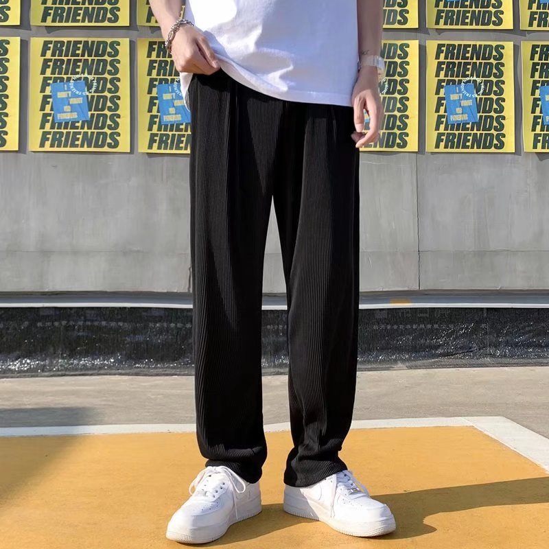 A man wearing black striped ice silk leggings and a white t-shirt, standing in front of a wall with 'FRIENDS' themed decorations.